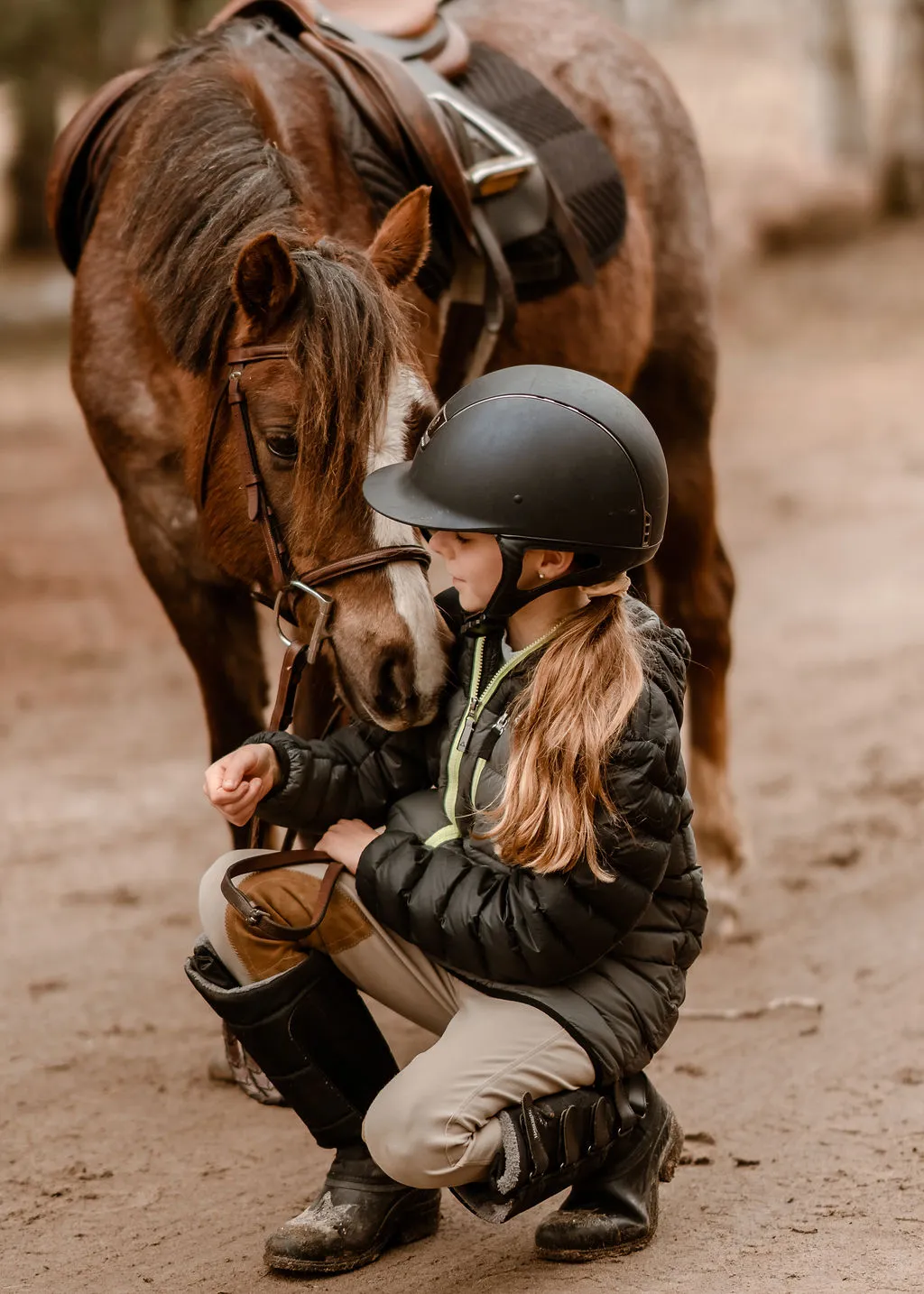 A young athlete kneels to bond with her pony