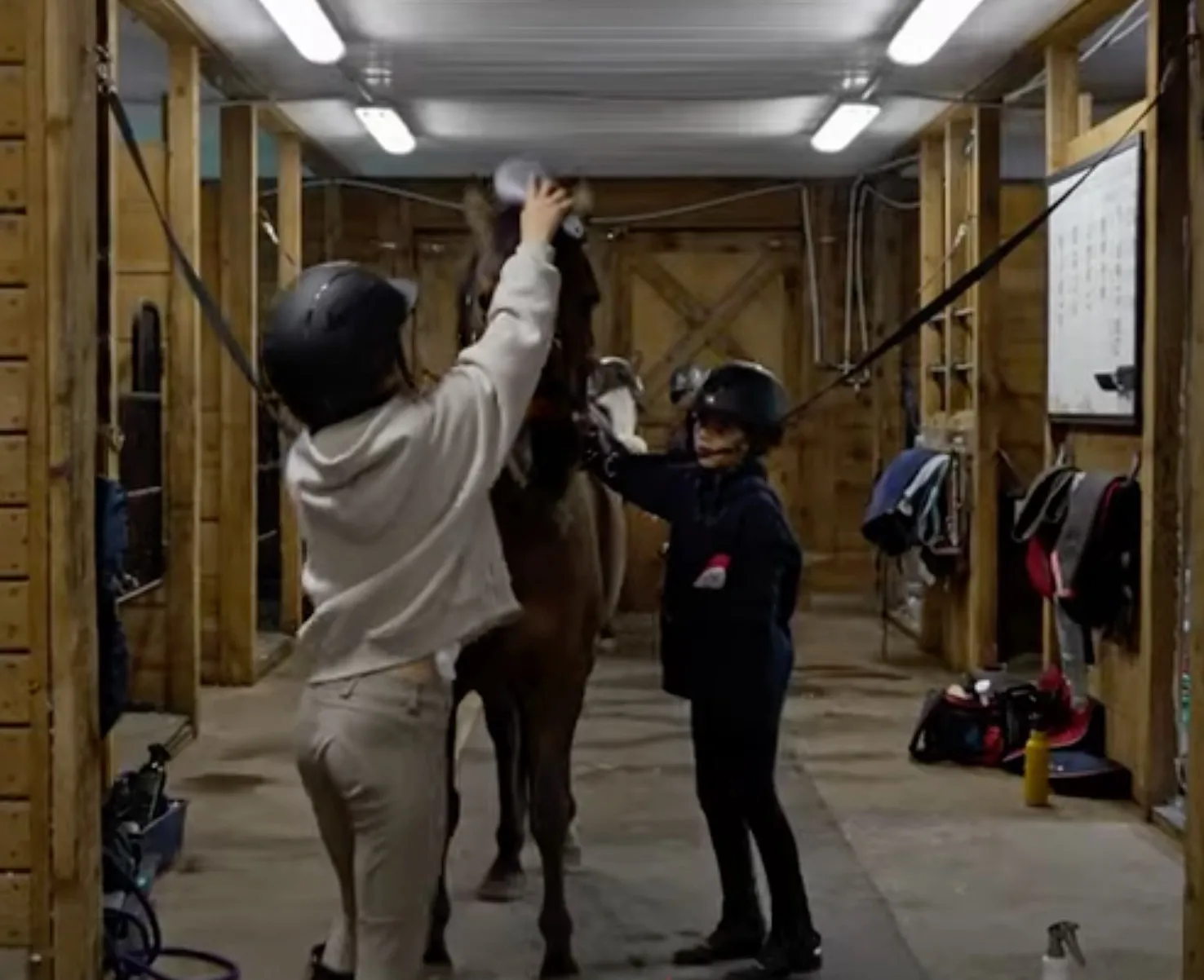 Two young athletes groom their pony in the barn aisle