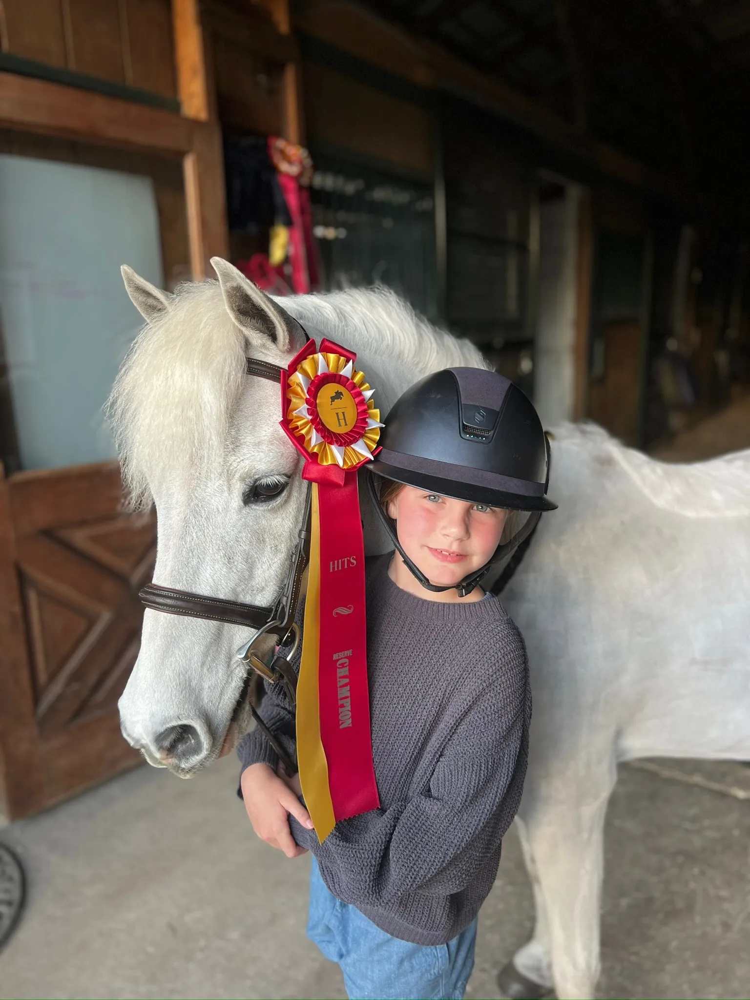 A young athlete cheek-to-cheek with a champion pony in the barn