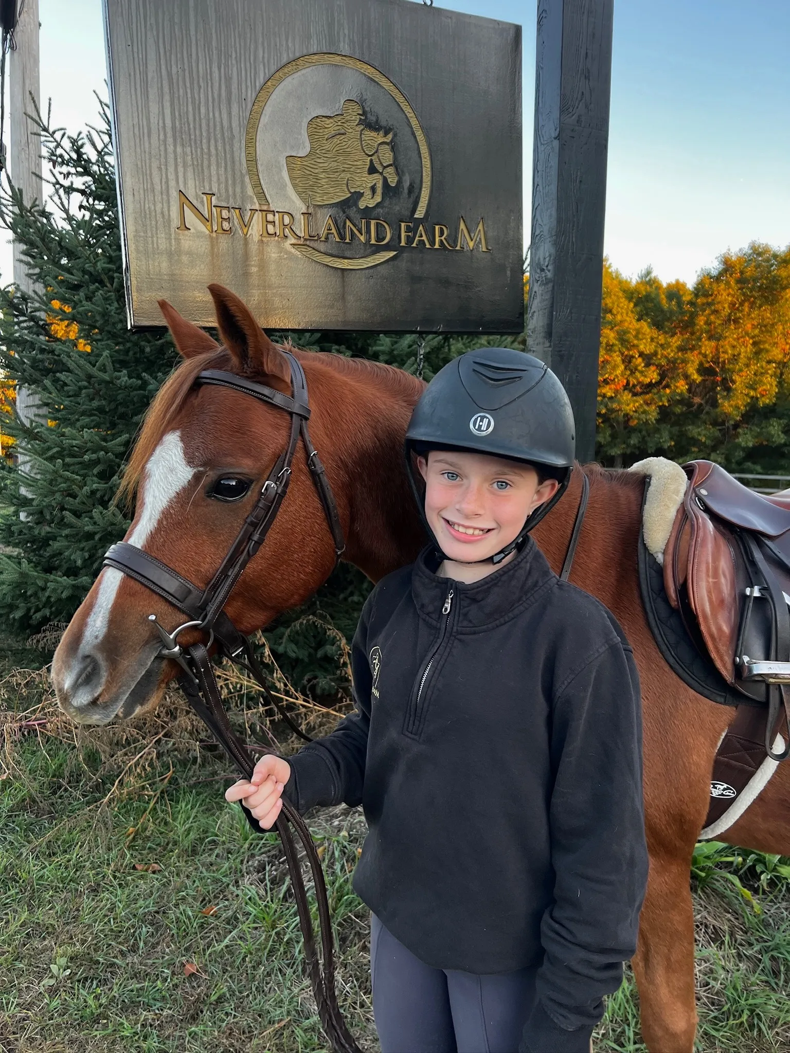 A young athlete and her pony at the Neverland Farm sign in autumn