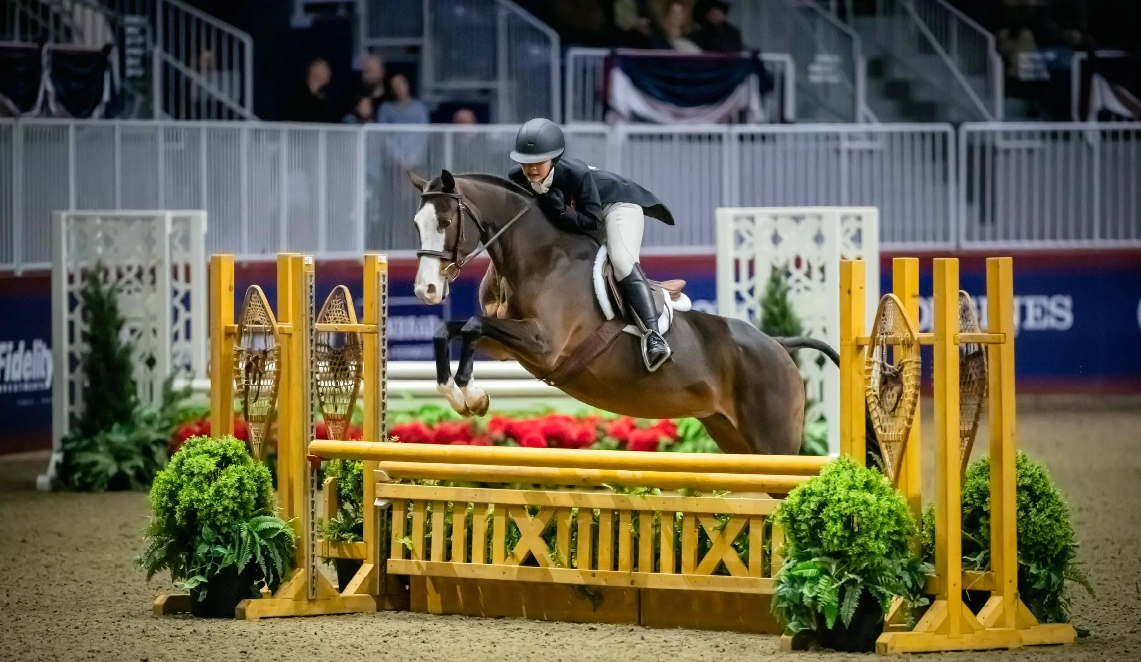 A young athlete and pony clear a decorated oxer at a championship show